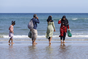 Famille, fillette, homme au téléphone et femmes voilées devant la mer à Skagen au Danemark.