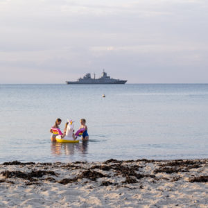 Navire militaire à l'horizon sur la mer et enfants jouant avec une grosse bouée sur une plage de la Mer du Nord en Allemagne.