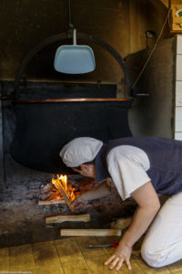 Une femme, fromagère, alimente le feu de bois sous le chaudron en cuivre pour le chauffage du lait et la fabrication du fromage, à la ferme Chez Valentin à Foncine-le-Haut