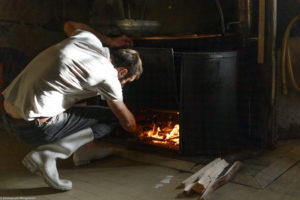 Un homme, fromager, ajoute du bois dans le feu sous le chaudron en cuivre dans la fromagerie de la ferme de Laisia dans le Haut-Jura
