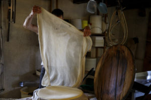 Un homme, fromager, change la toile d’égouttage du fromage qu’il vient de mouler dans la fromagerie de la ferme de Laisia dans le Haut-Jura
