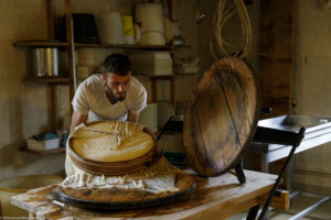 Un homme, fromager, retourne d’un geste sûr, le fromage qu’il vient de fabriquer dans la fromagerie de la ferme de Laisia dans le Haut-Jura