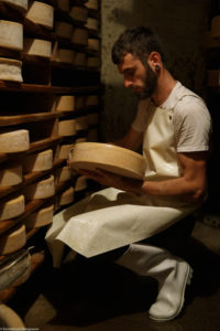 Un homme, fromager, soigne ses fromages dans la cave d’affinage de la ferme de Laisia dans le Haut-Jura
