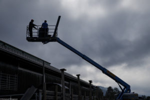Deux hommes sur une nacelle télescopique réparent le toit d'un bâtiment d'élevage avant l'hiver à Austbygde en Norvège