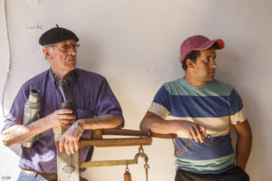 Deux hommes, un jeune avec une casquette rouge, un plus âgé avec un béret, maté sous le bras, suivent attentivement une vente aux enchères de fromages fermiers à Cardona en Uruguay.