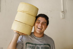 Portrait d'un jeune homme souriant qui porte trois meules de fromage sur l'épaule à Cardona en Uruguay.